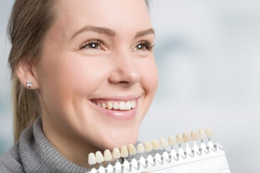 Woman comparing porcelain veneer shades with a dental shade guide