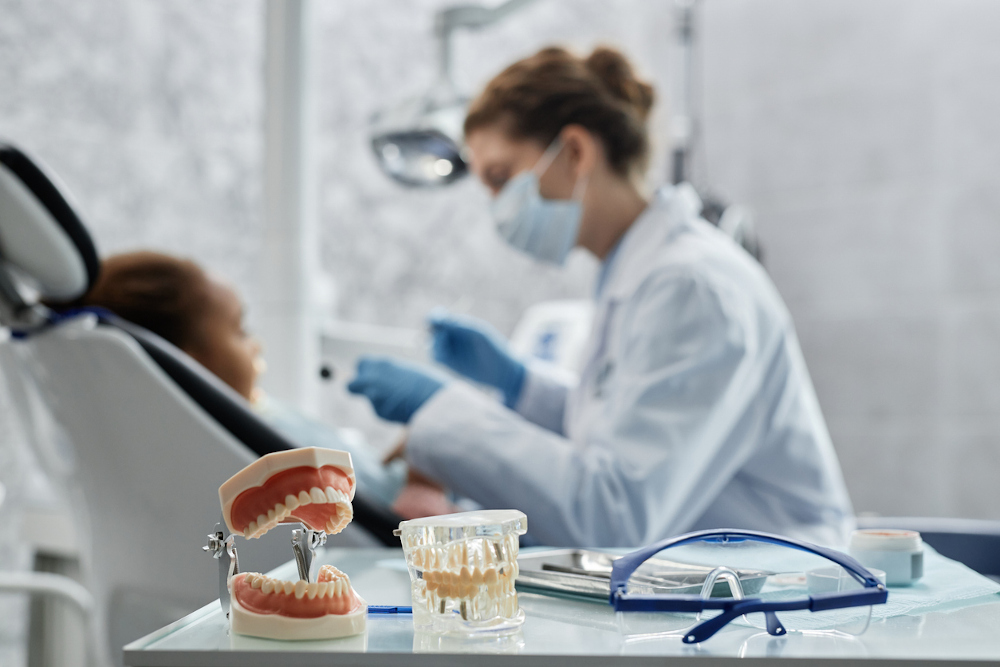 Dental implant models on tray with dentist consulting a patient in the background at a dental clinic