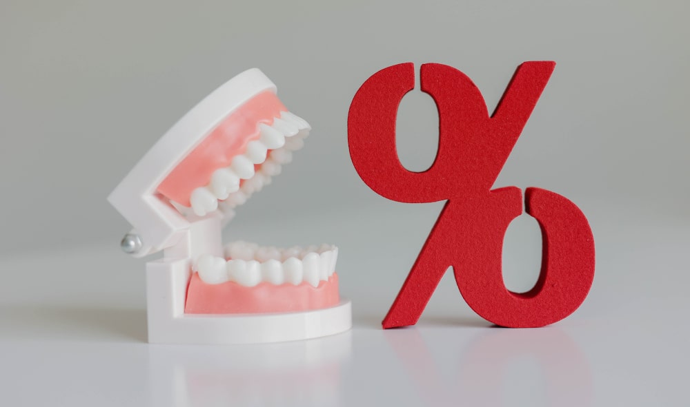 Dental jaw model with red percent sign symbolizing denture costs