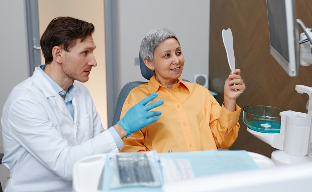 Senior woman looking in a mirror at a dental clinic while considering dental implant options and eligibility