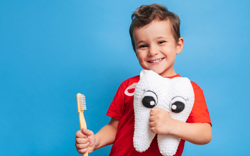 Happy child showing healthy teeth and holding a plush tooth, representing good dental health and prevention of tooth sensitivity.