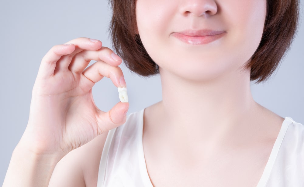 Smiling Woman Holding Removed Wisdom Tooth Happy woman smiling after successful wisdom tooth extraction